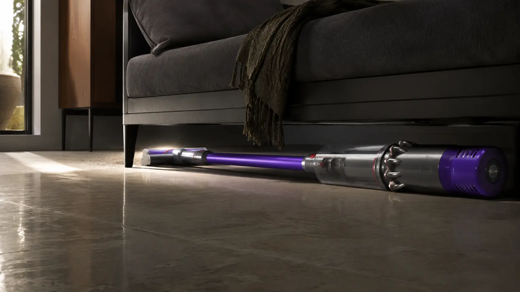 Dyson cordless vacuum reaching underneath a low sofa