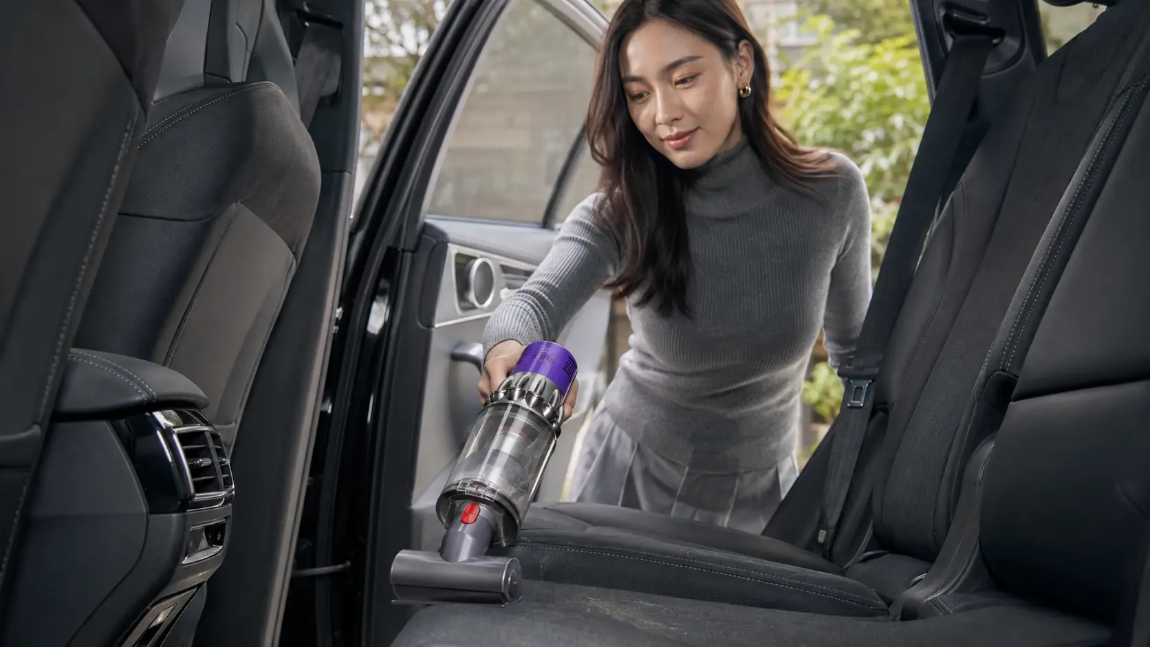 Woman using a Dyson cordless vacuum in a car interior